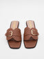 Flat brown sandals with gold buckle and square toe.